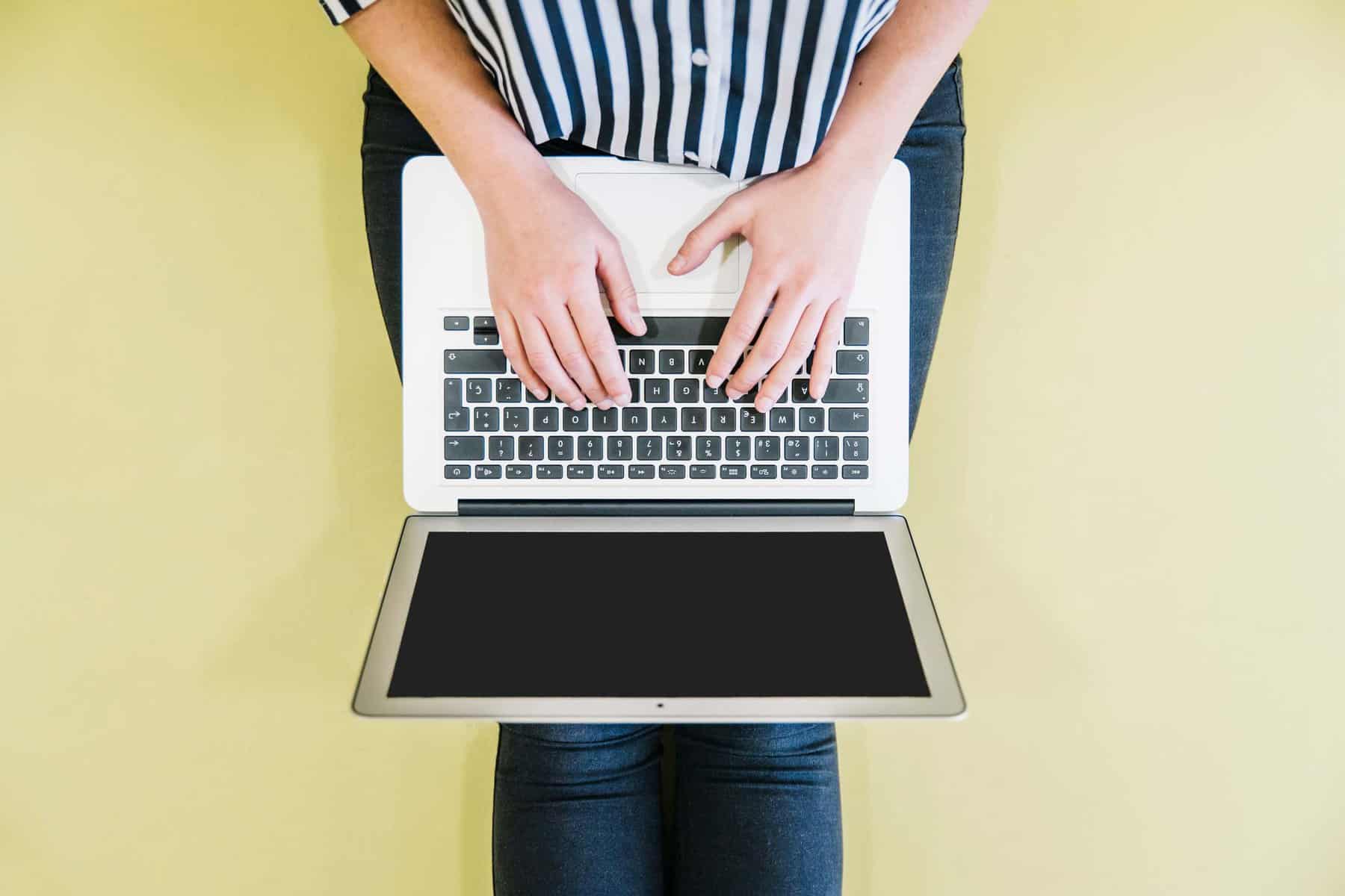 over head view of woman on laptop yellow background